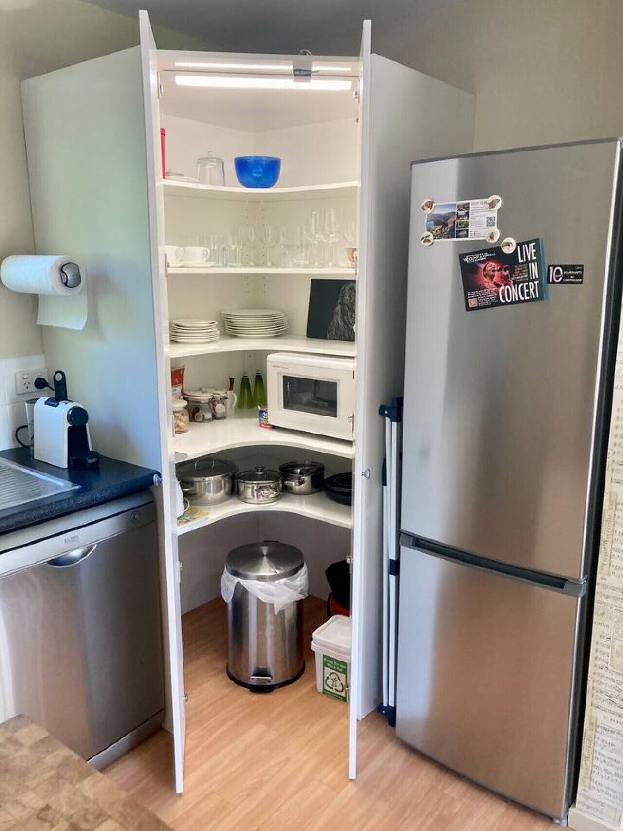 A compact kitchen with a built-in microwave, a stainless steel refrigerator, and a small trash bin.