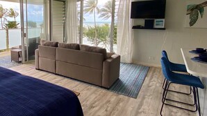 A room with a sofa, a TV mounted on the wall, and a balcony with a view of the ocean. - Beachfront & Oceanviews - New Furnishings (Hauula)
