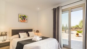 Un dormitorio moderno con una cama grande, dos mesitas de noche, una lámpara auxiliar, un cuadro y vistas al exterior a través de un ventanal corredera.