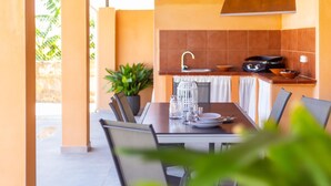 Cocina exterior con mesa para dos, una planta en maceta y vista a follaje.