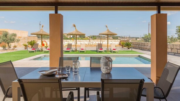 Un área de comedor al aire libre con piscina, sillas y sombrillas.
