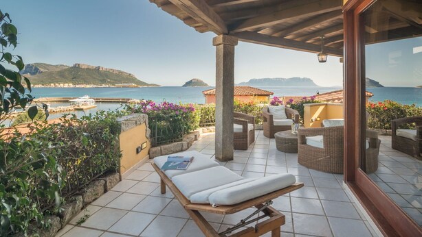 A covered outdoor seating area with wicker furniture, a wooden bench, and a view of the sea and hills. - Beautiful apartment for 6 people with WIFI, A/C, pool, TV, terrace and pets allowed (Regia Dogana)