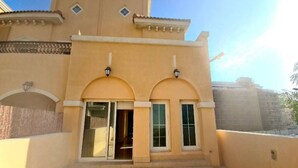 Un bâtiment à la façade beige, doté de deux fenêtres en arc surmontées de portes vitrées et d’un petit balcon.