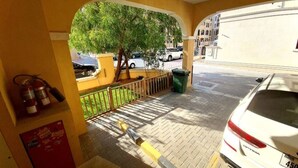 Un espace extérieur abrité, doté d’un mur jaune, d’un extincteur, d’une poubelle et d’une voiture blanche garée à proximité.