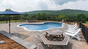 A swimming pool with a stone patio, surrounded by lounge chairs and a table.