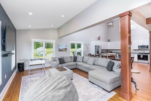 Amplia sala de estar con un sofá modular grande, una mesa de centro y una mesa de futbolín. Hay una zona de cocina con electrodomésticos modernos y una mesa de comedor.