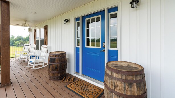 A porch with white railings, a blue door, and wooden barrels.