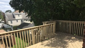 A wooden deck with a railing, a black mat, and a brick wall. - Private Apartment Near UBS Arena &JFK (Elmont)