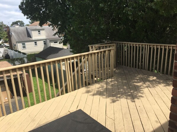 Una terraza de madera con barandilla, un tapete negro y un muro de ladrillo.