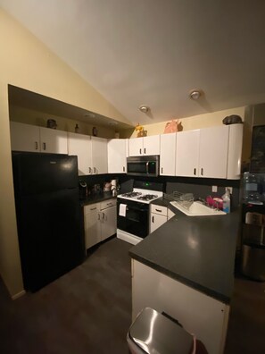 A kitchen with white cabinets, a black refrigerator, a microwave, and a stove.