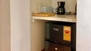 Ett litet kök med kylskåp, mikrovågsugn, kaffebryggare och en liten hylla med en kopp och en behållare.