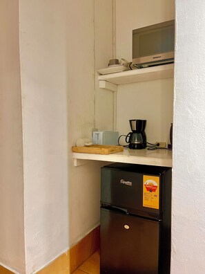 A kitchenette with a refrigerator, microwave, coffee maker, and a small shelf with a cup and a container. - Negril Beach Club studio D14 (Negril)
