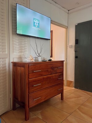 A wooden dresser with drawers, a flat-screen TV mounted above it, and a door in the background. - Negril Beach Club studio D14 (Negril)