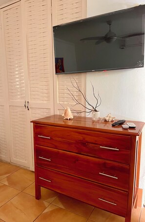 A wooden dresser with drawers, a television mounted on the wall, and a white closet with louvered doors. - Negril Beach Club studio D14 (Negril)