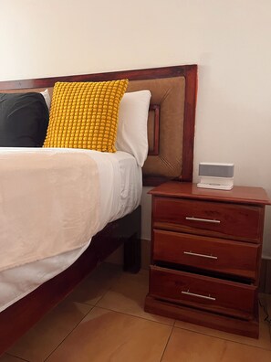 Ein Bett mit Holz-Kopfstück, ein Nachttisch mit Schubladen und eine digitale Uhr.