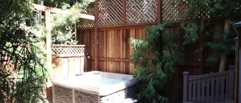 Un bain à remous dans un jardin, avec une clôture en bois et une pergola.