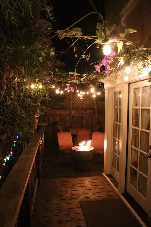 Une terrasse extérieure dotée d’un foyer, d’une plateforme en bois et de guirlandes lumineuses.