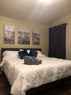 A neatly made bed with white linens and blue pillows, a woven basket with a towel, and three abstract paintings on the wall. - Charming Private Oasis- Approx 10 min to strip, Arcade Machine,FootMassagers (North Las Vegas)