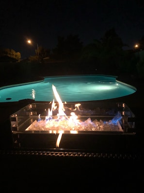 A swimming pool at night with a fire feature in the foreground.