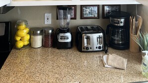 Una cocina con armarios blancos, encimera de granito, cafetera, tostadora, licuadora y una planta en el estante.