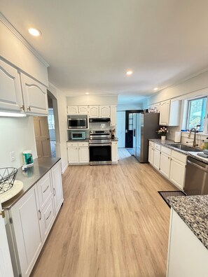 A modern kitchen with white cabinetry, stainless steel appliances, and a wooden floor.