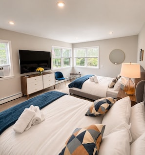 A bedroom with two beds, a TV, a desk, a chair, and a lamp.