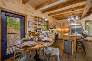 Cocina tipo cabaña de madera con comedor, armarios de madera, refrigerador de acero inoxidable y un taburete de bar.