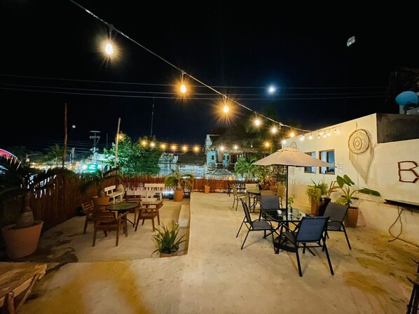 An outdoor patio area with string lights, tables, chairs, and potted plants.