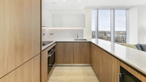Eine moderne Küche mit Holzausstattung, einer weißen Arbeitsplatte und Blick auf die Stadt durch große Fenster.
