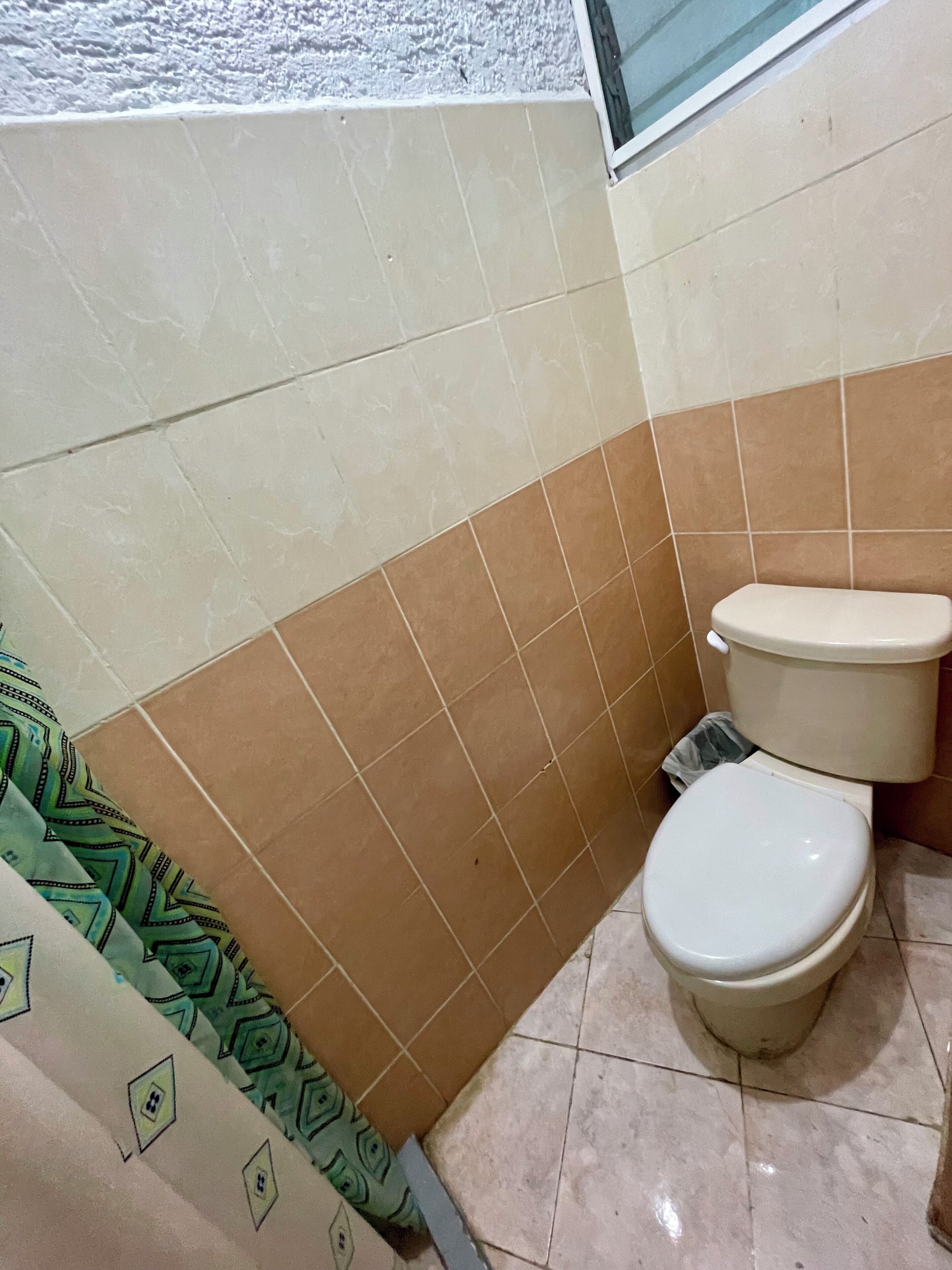 Une salle de bain avec deux toilettes, un carrelage au sol et un rideau à motifs.