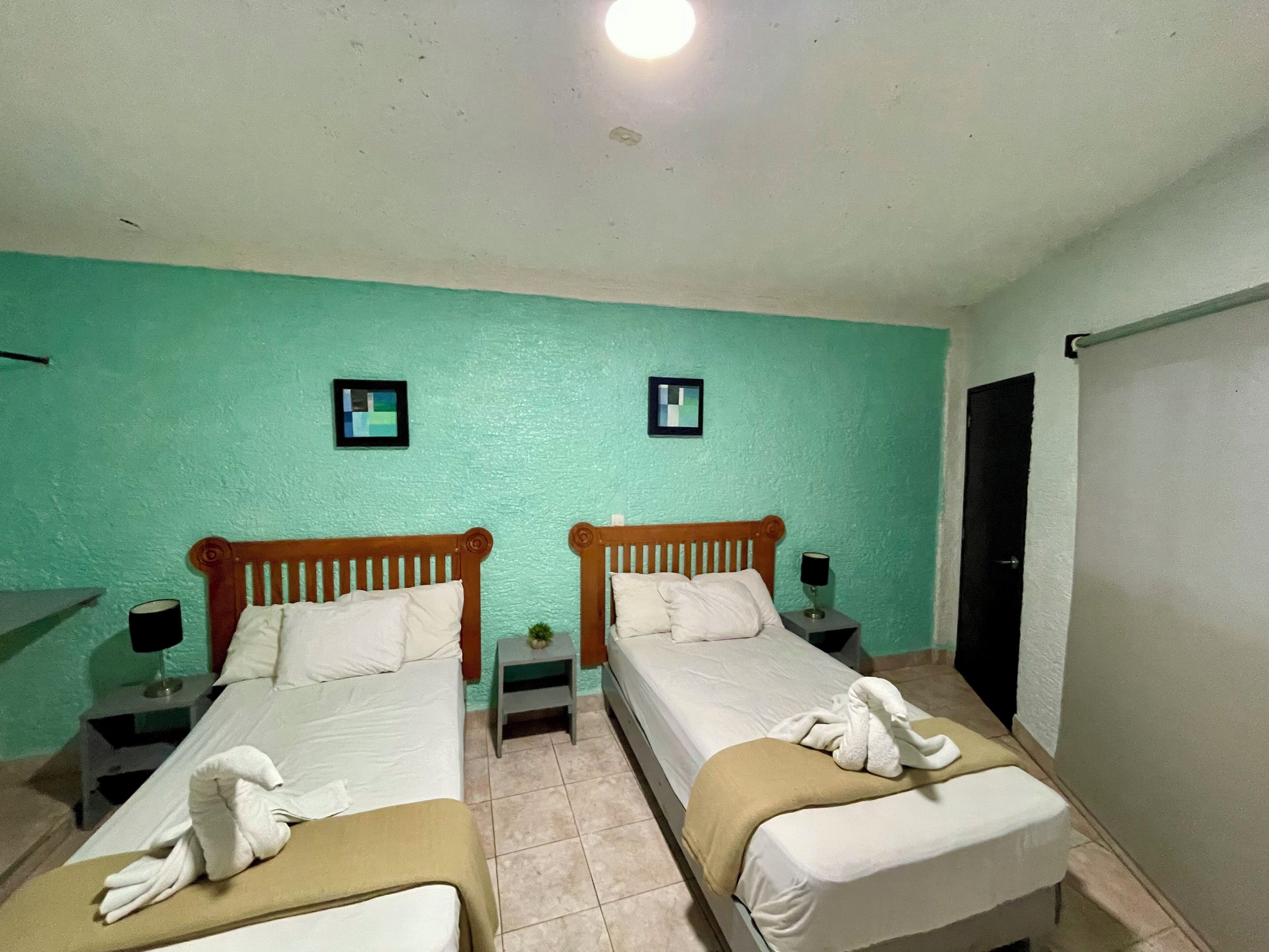 Ein Doppelzimmer mit zwei Betten, einem kleinen Tisch, einem Nachttisch und einem an der Wand befestigten Fernseher.