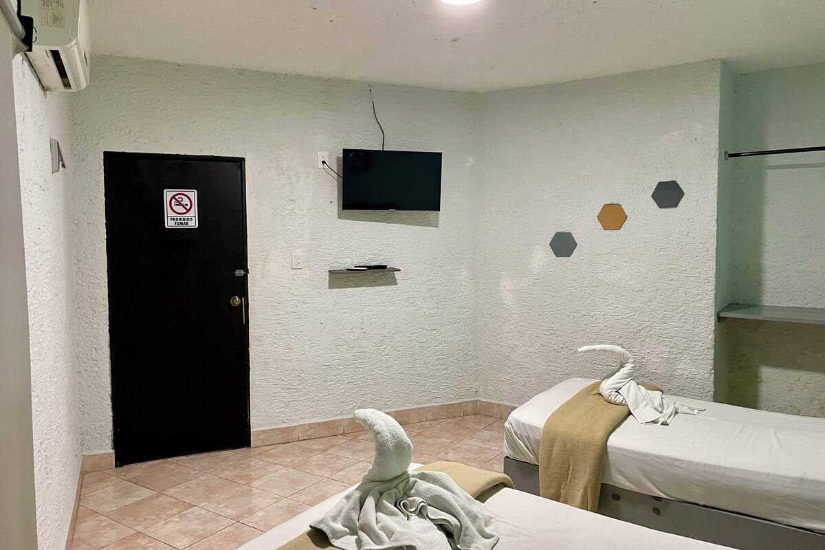 Hotellihuone, jossa on kaksi sänkyä, seinälle asennettu televisio, ovi, jossa on tupakointikielto-merkki, ja pieni hylly.