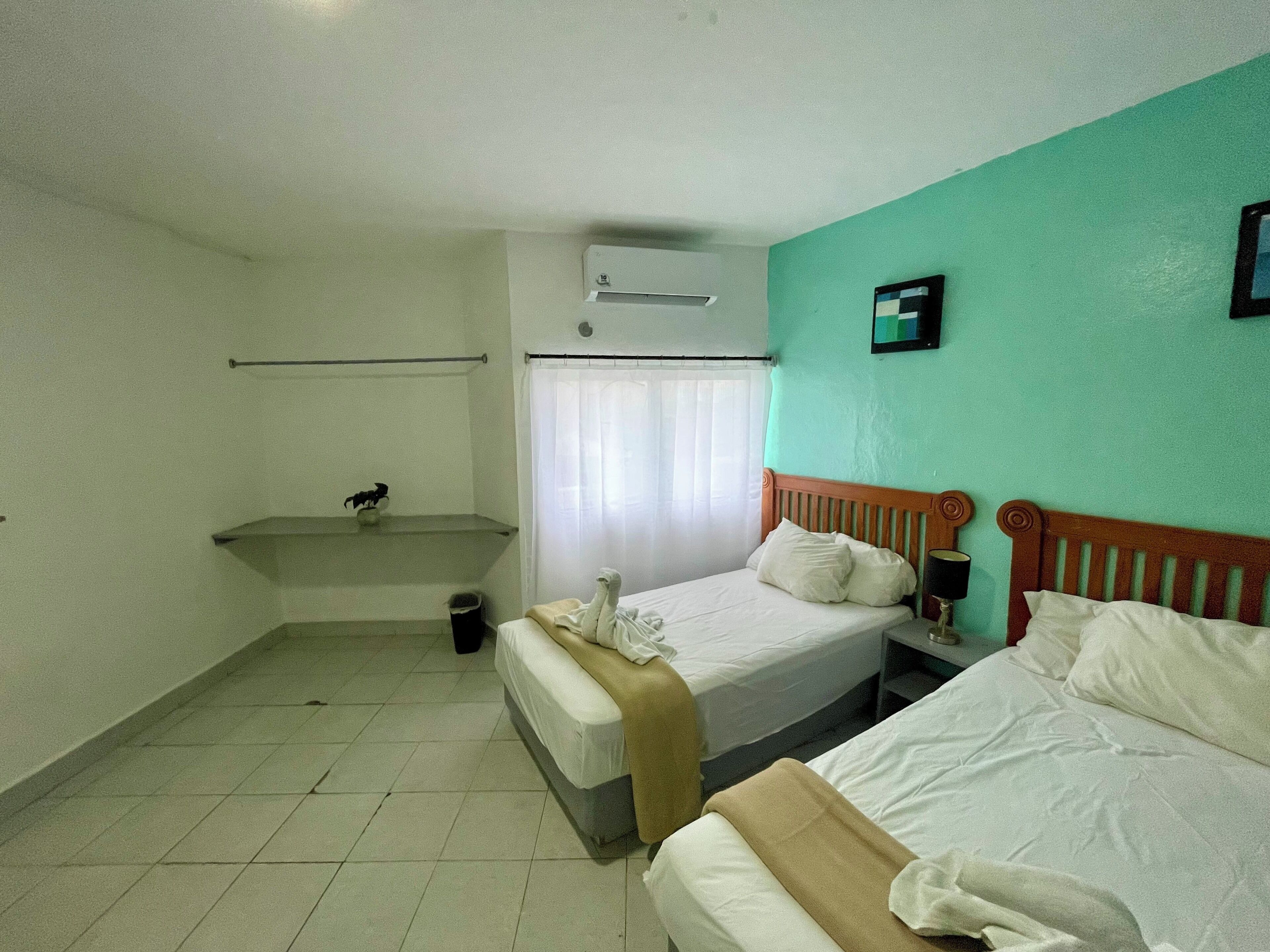 Une chambre d’hôtel avec deux lits, une petite salle de bain et une fenêtre avec des rideaux.