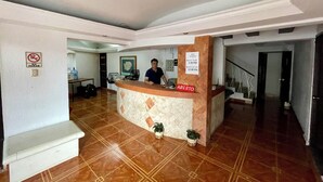 Zona de recepción de un hotel con mostrador de check-in, un cartel de prohibido fumar y un letrero con los horarios de entrada y salida.