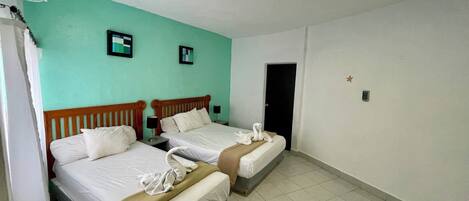 A hotel room with two beds, a teal-colored wall, a door, and a ceiling light.