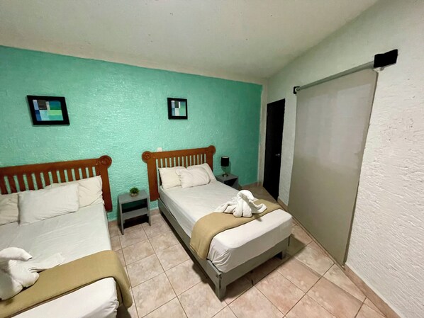 Une chambre avec deux lits, une petite table, une table de chevet, un miroir et une porte.