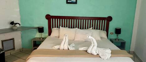 A neatly made bed with white linens and two decorative swans, a wooden headboard, two wall-mounted picture frames, and bedside lamps on a teal-colored wall.