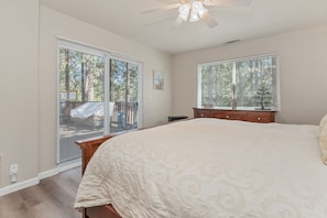 A bedroom with a large bed, a ceiling fan, a dresser, and two windows with blinds.