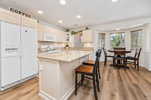 A modern kitchen with a central island, white cabinetry, and a dining area with wooden chairs.