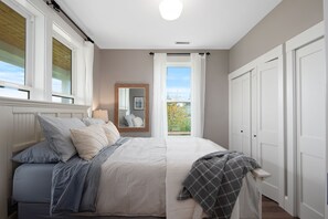 Quarto com cama grande, janela com cortinas, espelho e vista para o exterior.