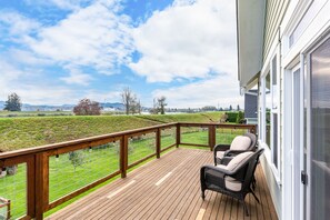 Um deck de madeira com guarda-corpo, duas cadeiras de vime e vista para uma paisagem verde.