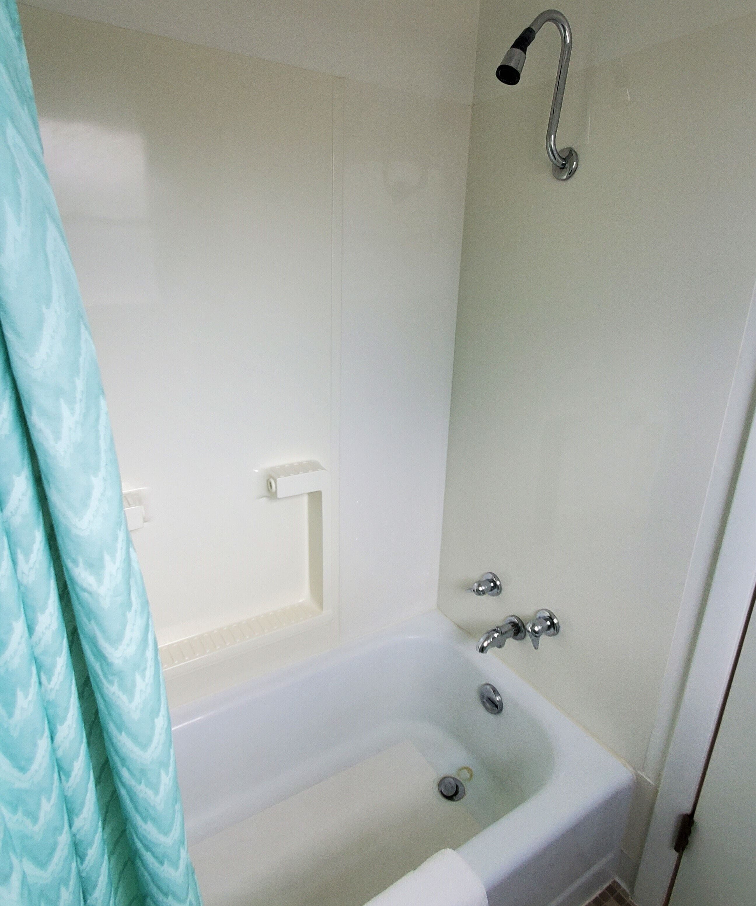 Un baño con una bañera blanca, un cabezal de ducha y un perchero para toallas.