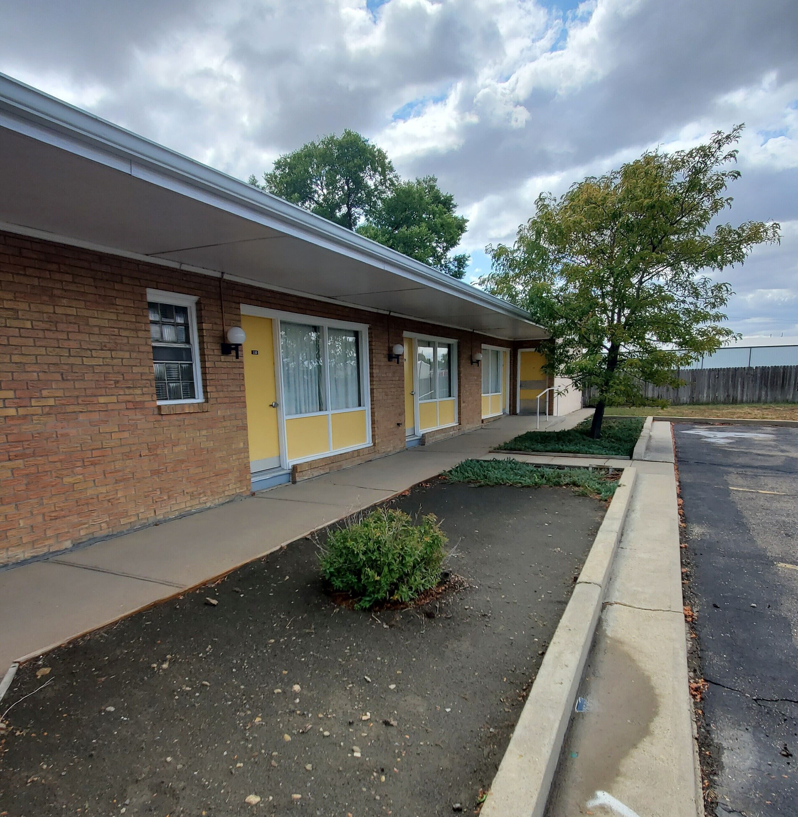 A row of motel rooms with a brick facade, yellow doors, and a small garden area in front.