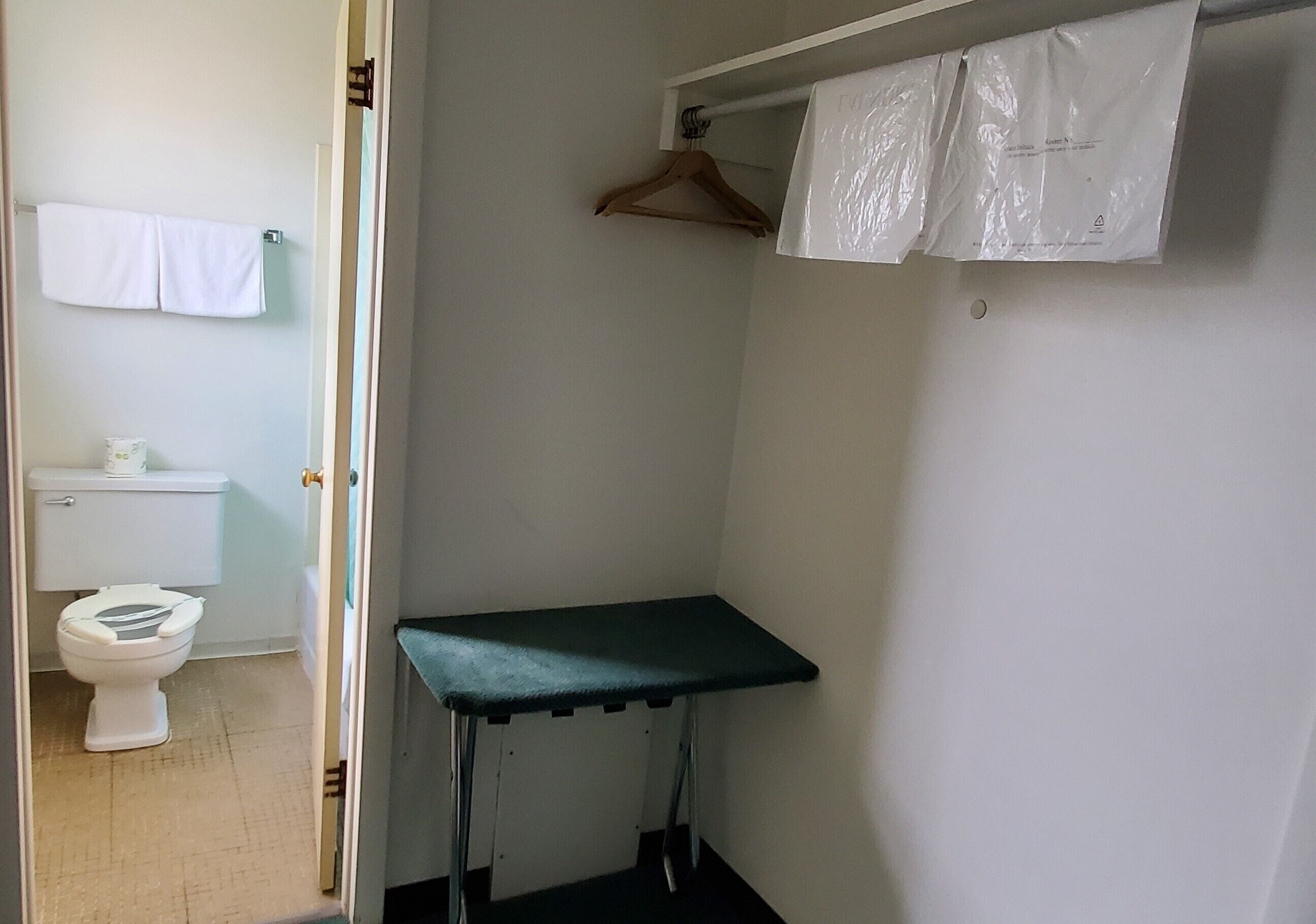 A small bathroom with a toilet, a towel hanging on the wall, and a green shelf.