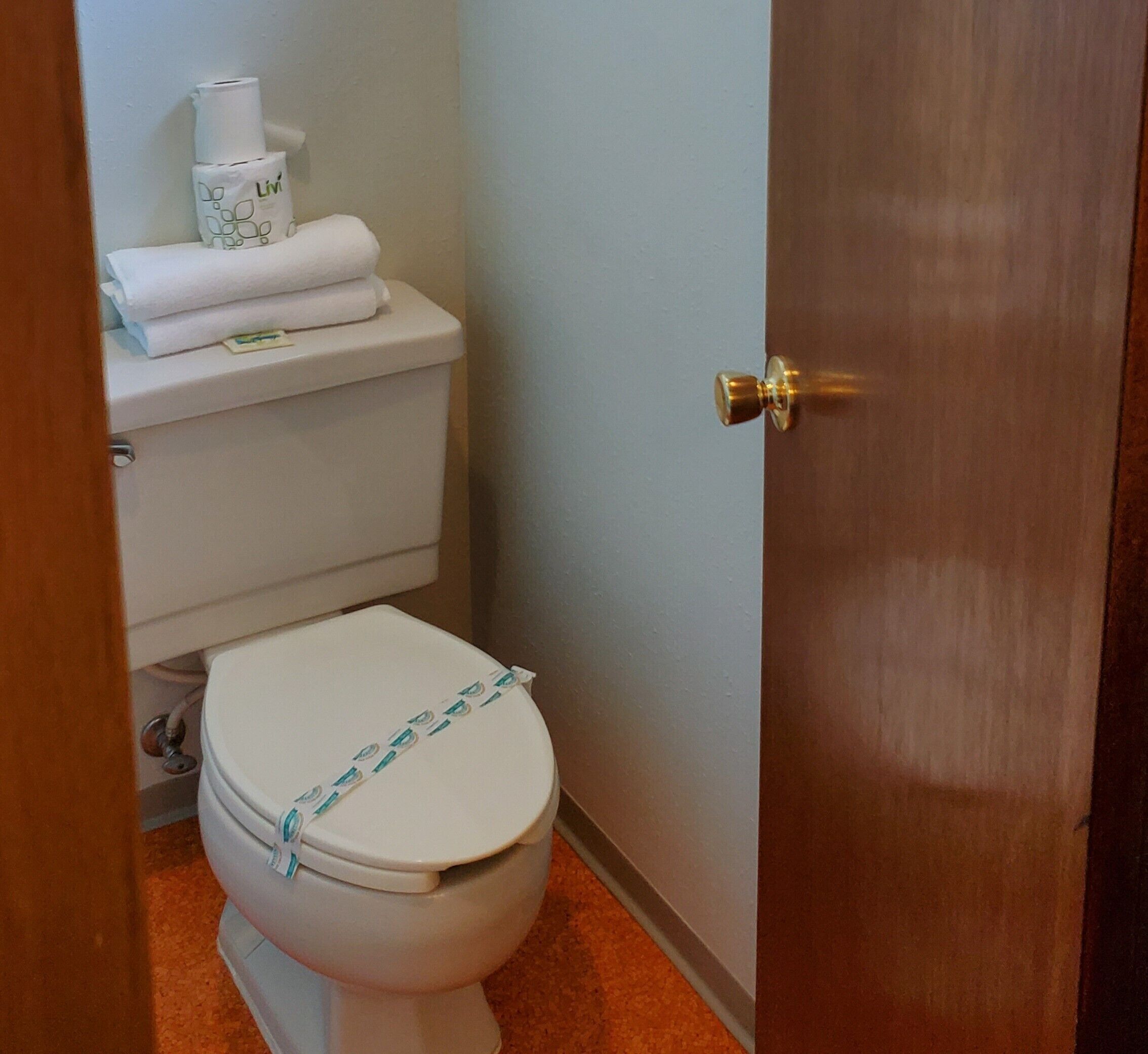 A bathroom with a toilet, a roll of toilet paper, and a bottle of hand soap on the wall.