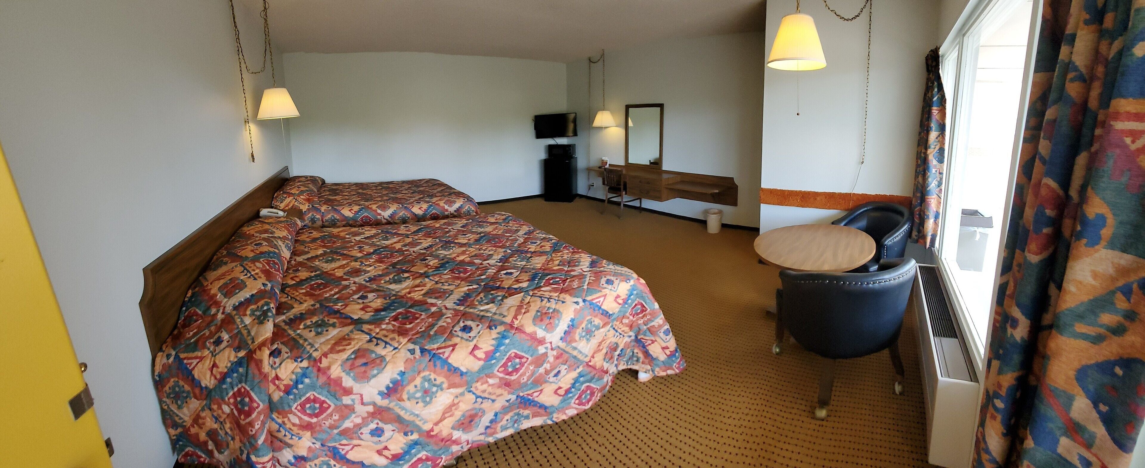 A hotel room with two beds, a desk, a chair, a TV, and a window with curtains.