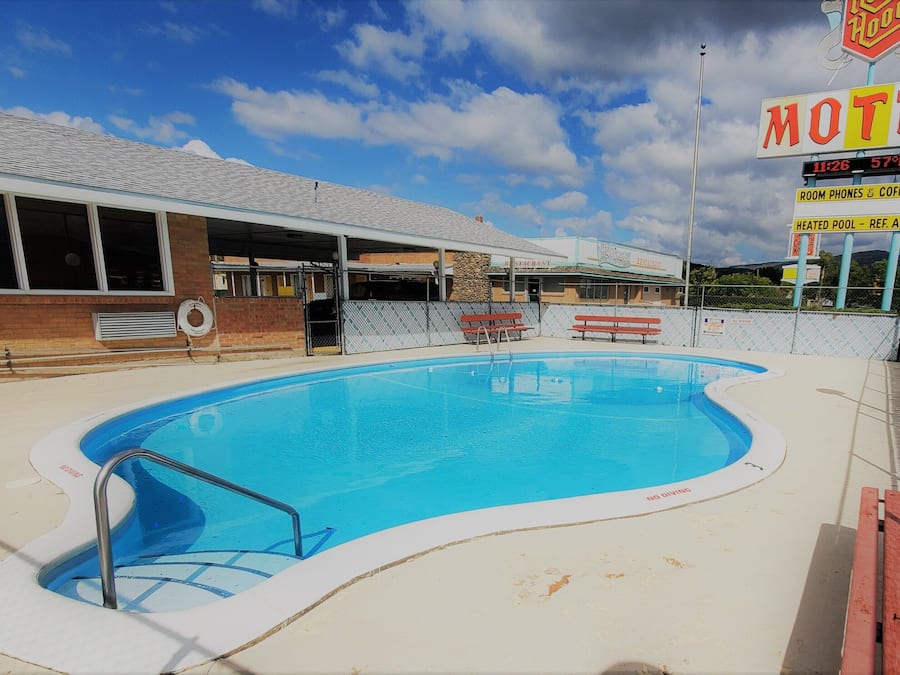 A motel with a swimming pool, a covered area, and a sign indicating amenities like room phones and coffee.