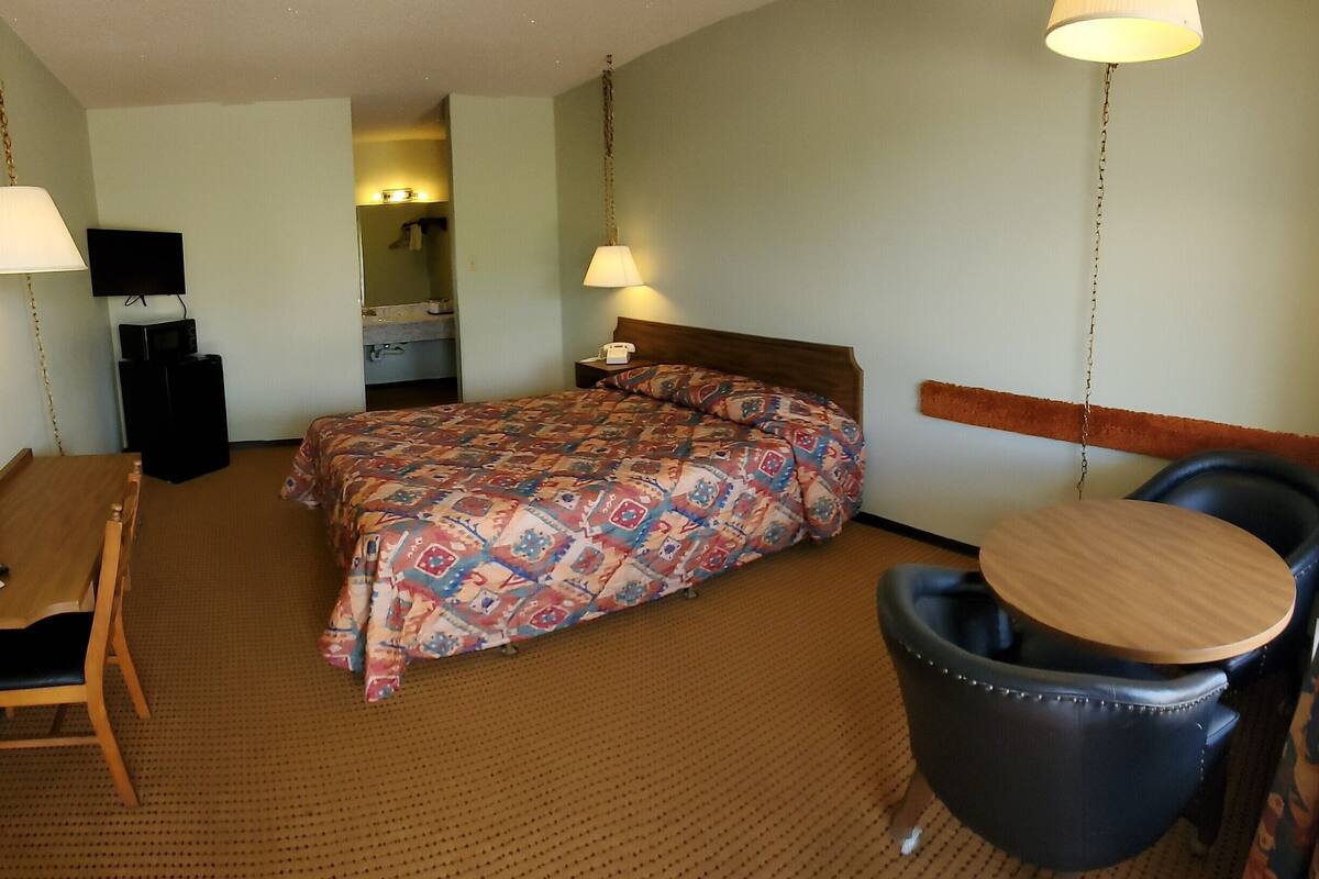 A hotel room with a bed, a desk, a chair, a small table, a mirror, and a television.