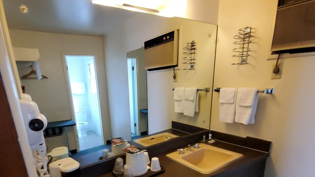 A hotel bathroom with a large mirror, two sinks, a hairdryer, and a towel rack.