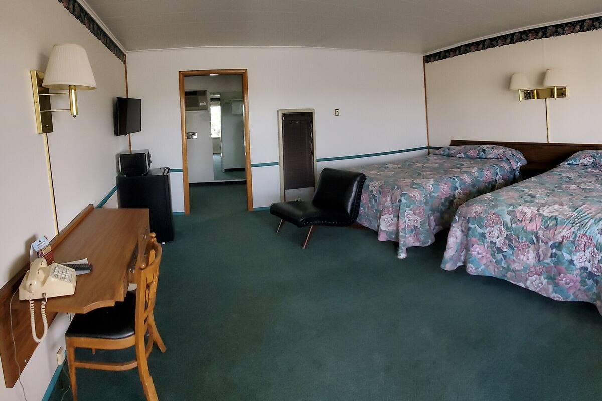 A hotel room with two beds, a desk with a telephone, and a mirror.